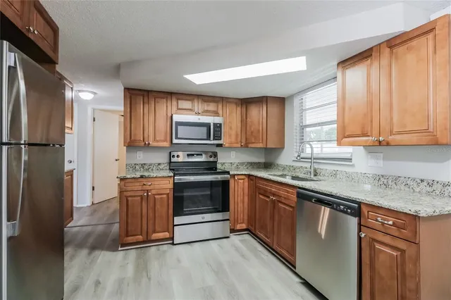 a kitchen with stainless steel appliances granite countertop a stove a sink dishwasher a refrigerator and a microwave oven with wooden floor