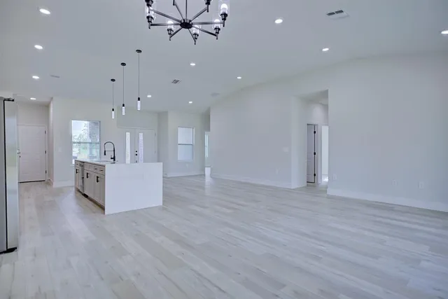 a view of an empty room with wooden floor and a kitchen