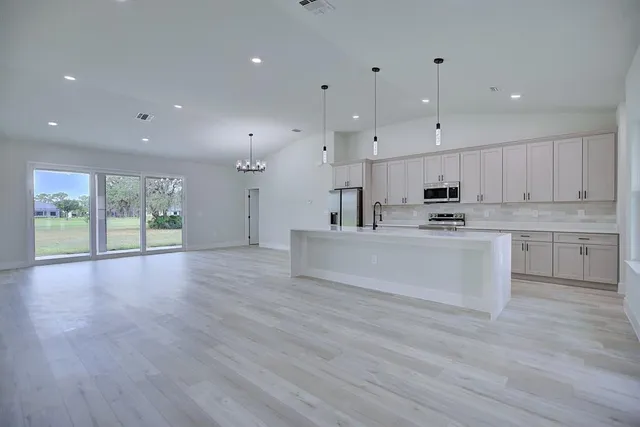 a large kitchen with stainless steel appliances a large counter top a stove a refrigerator with white cabinets and wooden floor