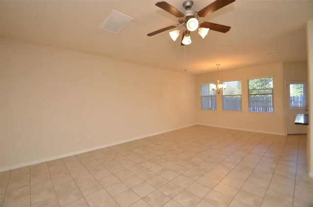 an empty room with chandelier fan and windows