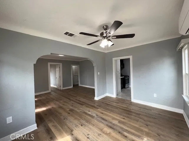a view of an empty room with wooden floor and a ceiling fan
