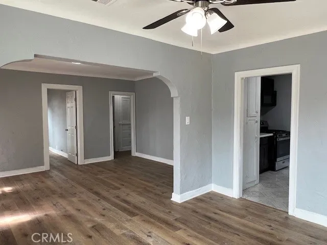 a view of an empty room with wooden floor and a ceiling fan