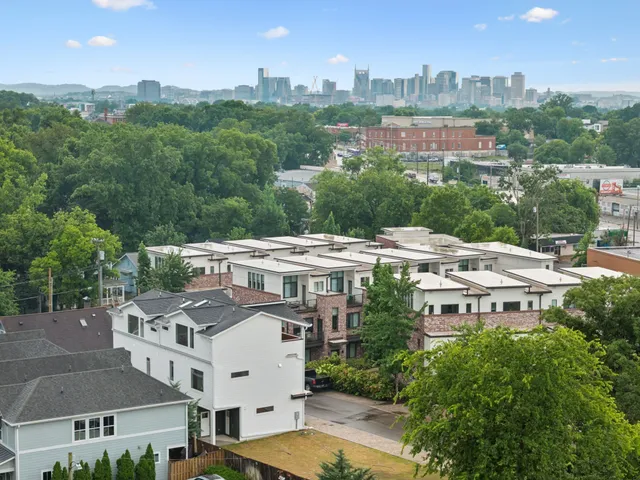 a view of a white building with a big yard plants and large trees