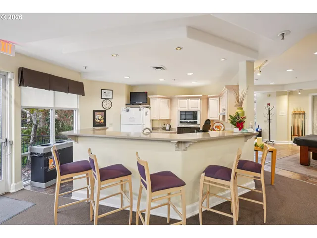 a kitchen with stainless steel appliances kitchen island granite countertop a dining table chairs and a refrigerator