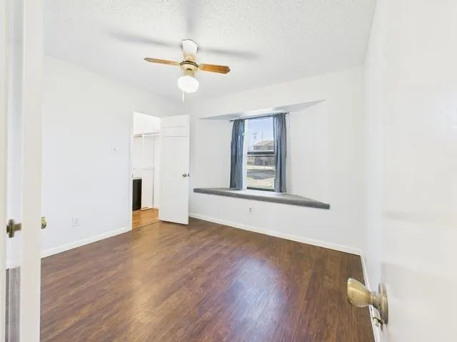a view of an empty room with wooden floor and a ceiling fan
