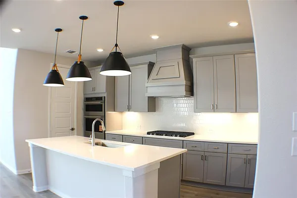 a kitchen with stainless steel appliances granite countertop a sink a stove a refrigerator and island with wooden floor