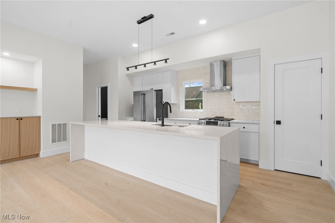 2155 Columbus Road Cleveland, OH 44113 - Photo 12 of 50 Kitchen with wall chimney range hood, freestanding refrigerator, light wood-type flooring, white cabinetry, and recessed lighting