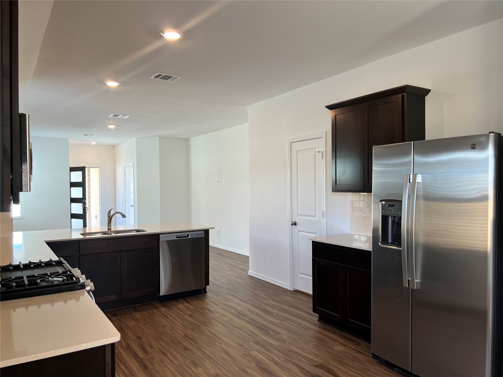 115 Canley Loop Hutto, TX 78634 - Photo 10 of 18 Kitchen featuring appliances with stainless steel finishes, dark brown cabinetry, light stone countertops, dark wood-style floors, and recessed lighting