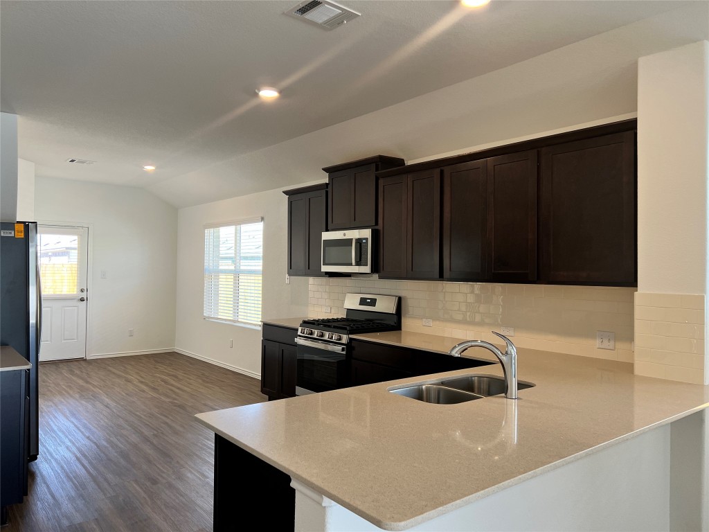 115 Canley Loop Hutto, TX 78634 - Photo 3 of 18 Kitchen featuring stainless steel appliances, a peninsula, lofted ceiling, light stone counters, and dark wood-type flooring