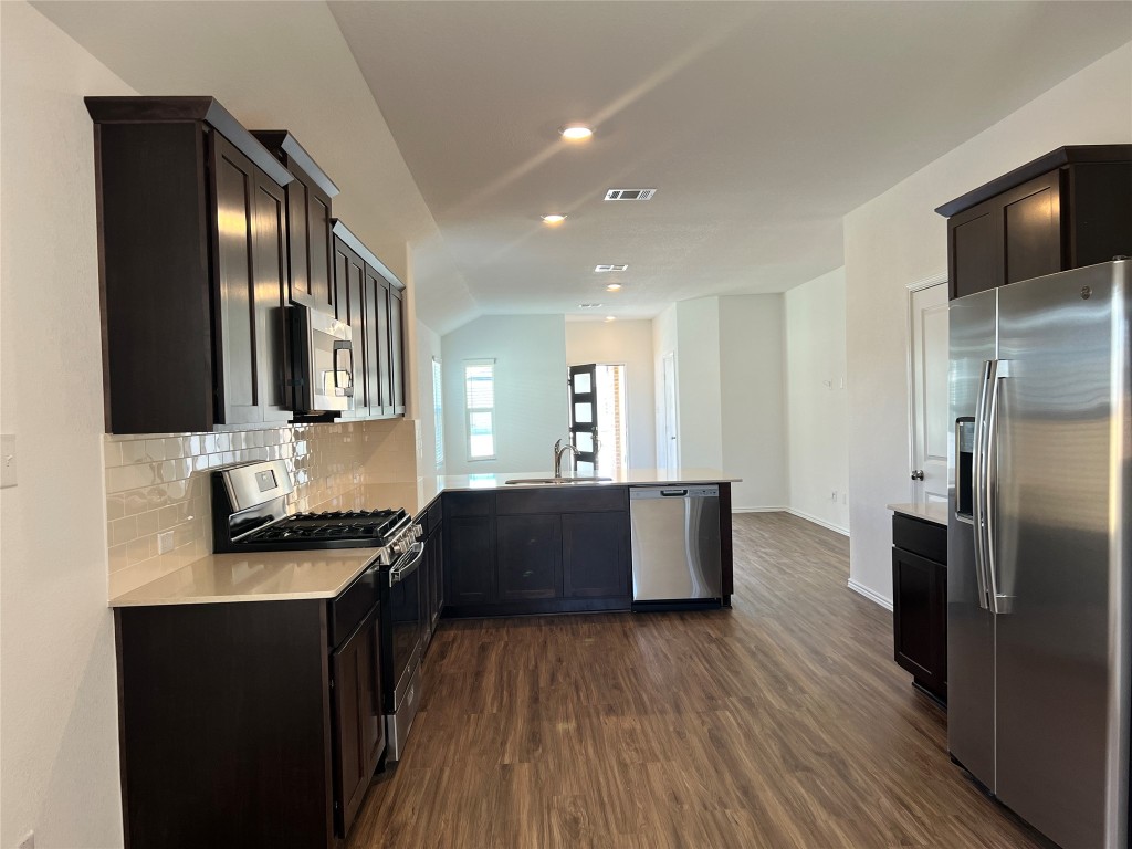 115 Canley Loop Hutto, TX 78634 - Photo 9 of 18 Kitchen featuring appliances with stainless steel finishes, backsplash, dark wood-type flooring, a peninsula, and vaulted ceiling