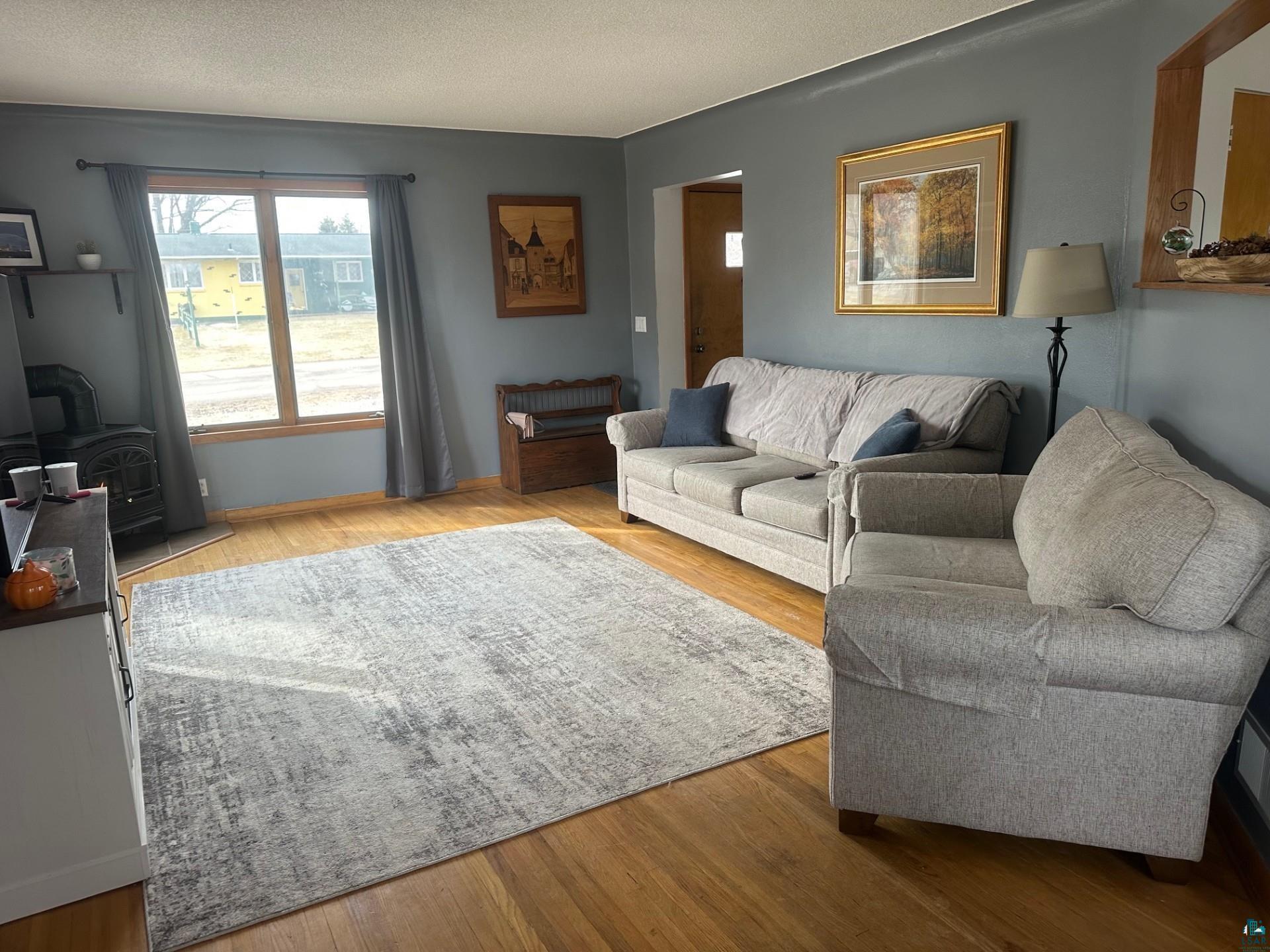 702 27th Street Cloquet, MN 55720 - Photo 2 of 25 Living room with light wood finished floors, a textured ceiling, and a wood stove