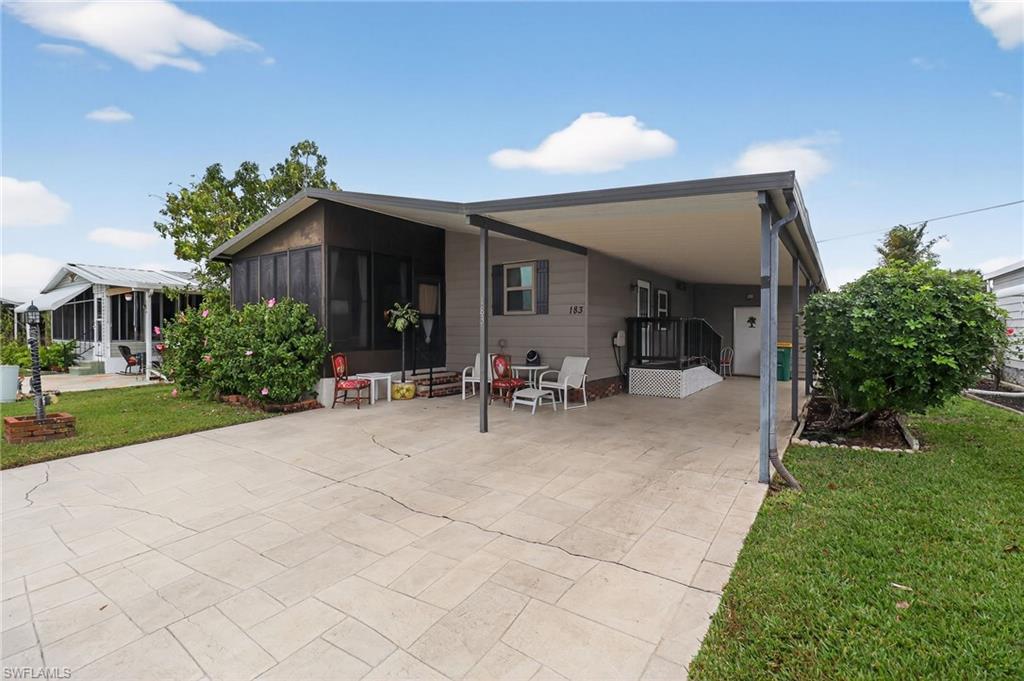 183 Oceans Boulevard, Unit 183 Naples, FL 34104 - Photo 2 of 28 Rear view of property featuring a yard, a carport, a sunroom, and driveway