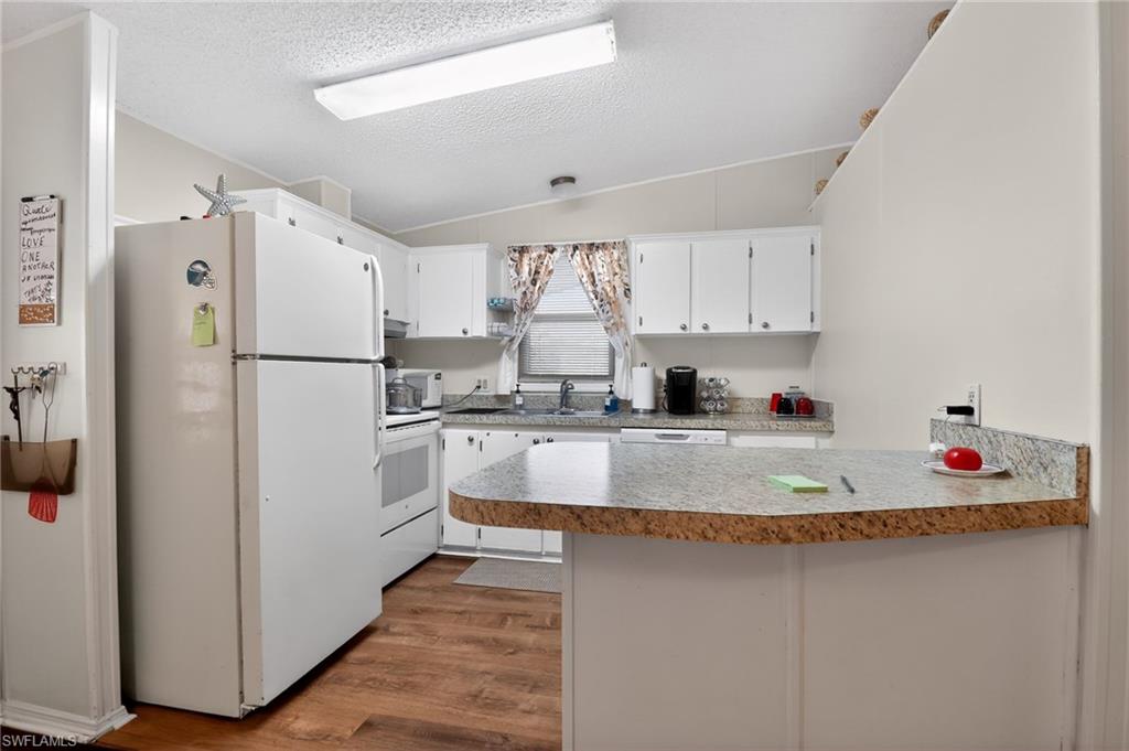 183 Oceans Boulevard, Unit 183 Naples, FL 34104 - Photo 7 of 28 Kitchen featuring white cabinets, a peninsula, white appliances, light countertops, and dark wood-style floors