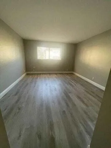 a view of an empty room with wooden floor and window