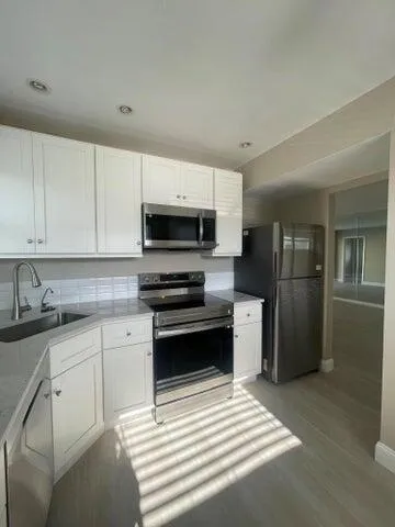 a kitchen with stainless steel appliances granite countertop white cabinets and a stove a sink
