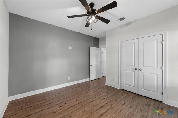 a view of an empty room with window a ceiling fan and wooden floor