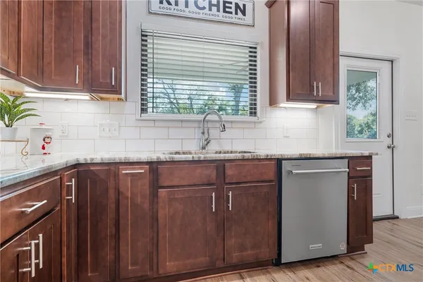 a kitchen with granite countertop wooden cabinets a sink and dishwasher next to a window