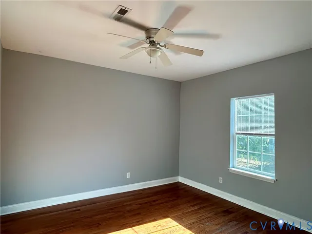 a view of an empty room with wooden floor and a ceiling fan