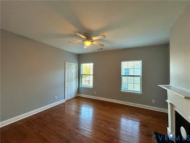 an empty room with wooden floor a ceiling fan and windows
