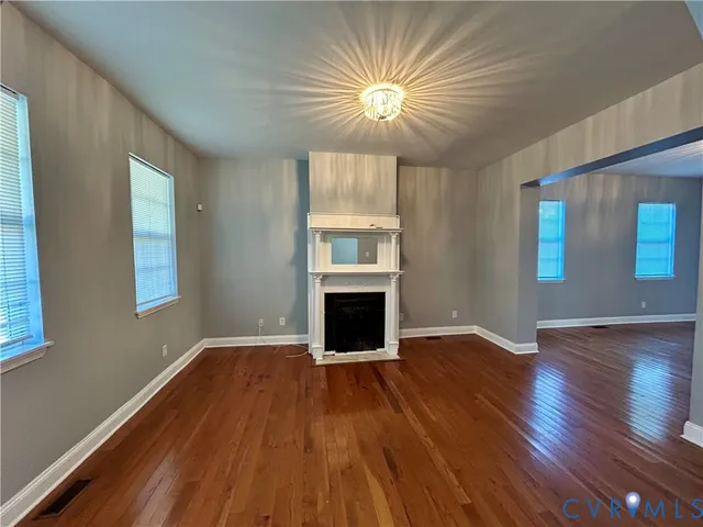 an empty room with wooden floor fireplace and windows