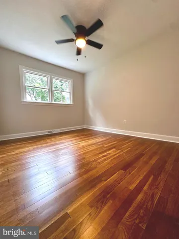an empty room with wooden floor chandelier fan and windows