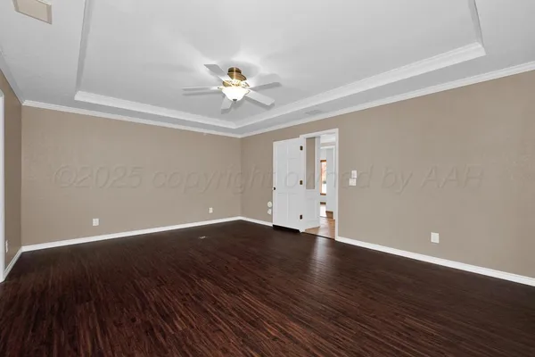 a view of an empty room with wooden floor and a ceiling fan