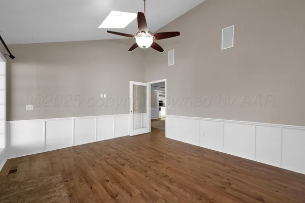 a view of an empty room with wooden floor and a ceiling fan