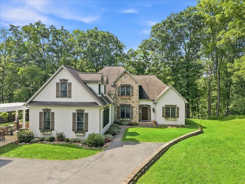 Mature trees frame a classic stone and stucco facade overlooking a verdant lawn.