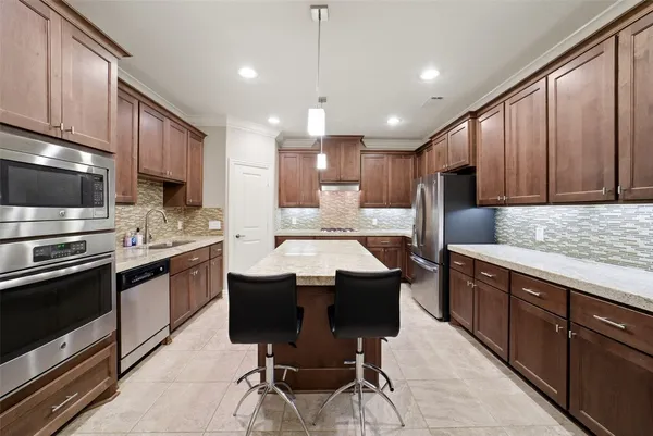 a kitchen with stainless steel appliances granite countertop wooden cabinets a sink dishwasher a stove a refrigerator and a oven with wooden floor