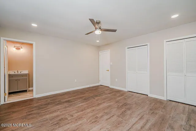 an empty room with wooden floor a ceiling fan and kitchen view