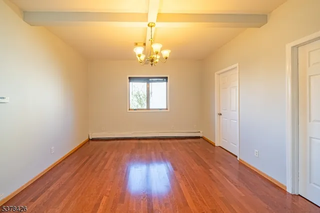 an empty room with wooden floor chandelier and window