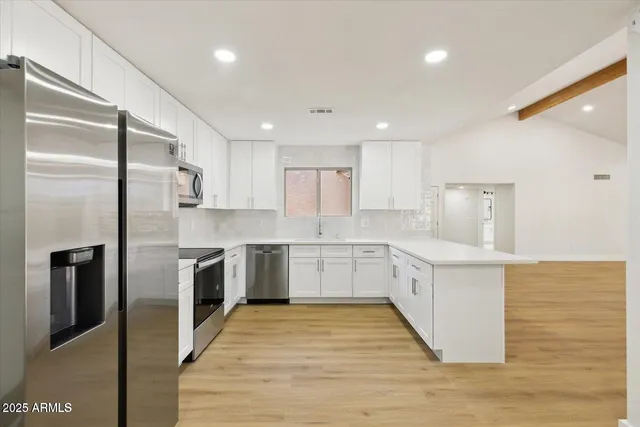 a large kitchen with stainless steel appliances cabinets a sink and a wooden floor