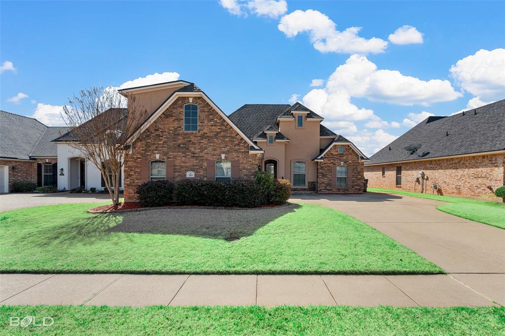Traditional-style home featuring a front yard, stucco siding, brick siding, and curved driveway
