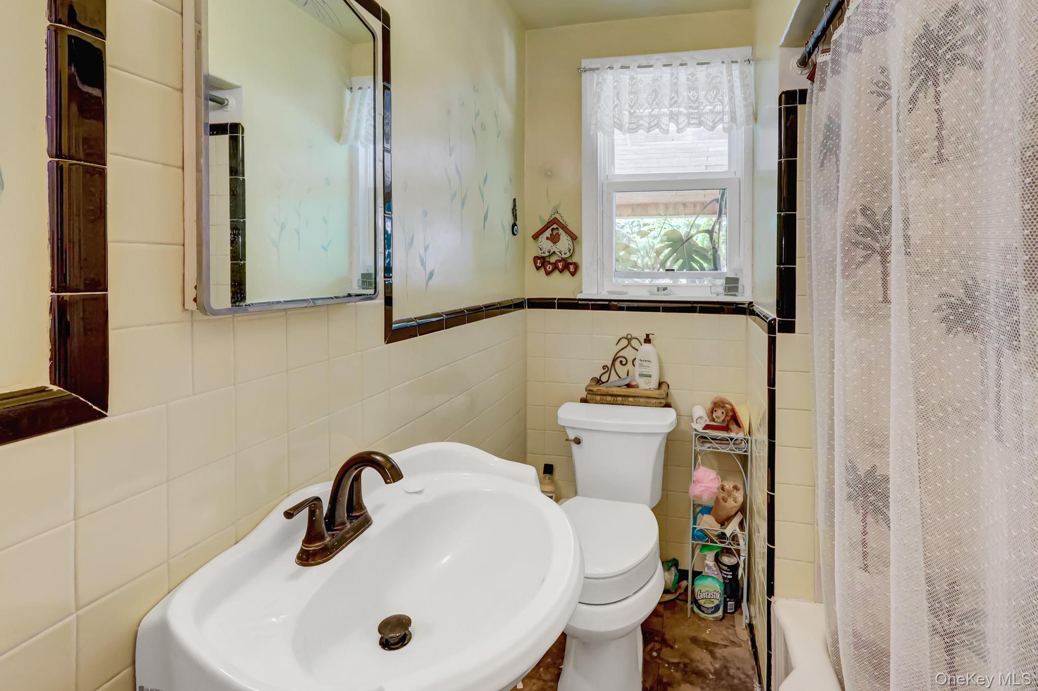 100 Elwood Road Northport, NY 11768 - Photo 18 of 39 Bathroom featuring a pedestal sink with a bronze-finish faucet, a mirrored medicine cabinet, a window with a valance, and wall tiling with a dark trim