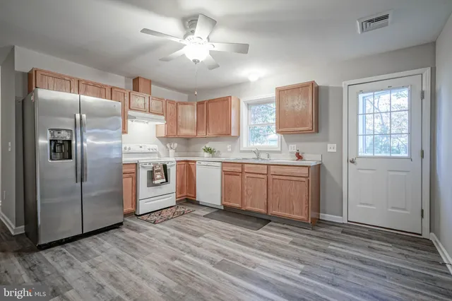 a kitchen with stainless steel appliances granite countertop a refrigerator a sink dishwasher a stove and white countertops with wooden floor