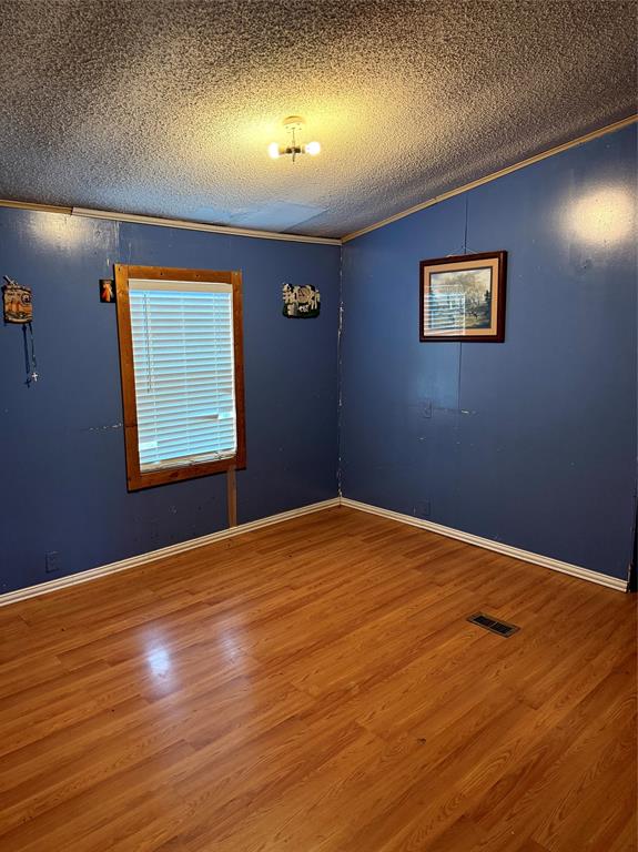 1047 John Wayne Road Kaufman, TX 75142 - Photo 11 of 17 Empty room featuring wood finished floors, crown molding, and a textured ceiling
