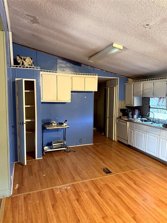 1047 John Wayne Road Kaufman, TX 75142 - Photo 12 of 17 Kitchen with vaulted ceiling, light wood-style floors, dishwasher, white cabinets, and a textured ceiling