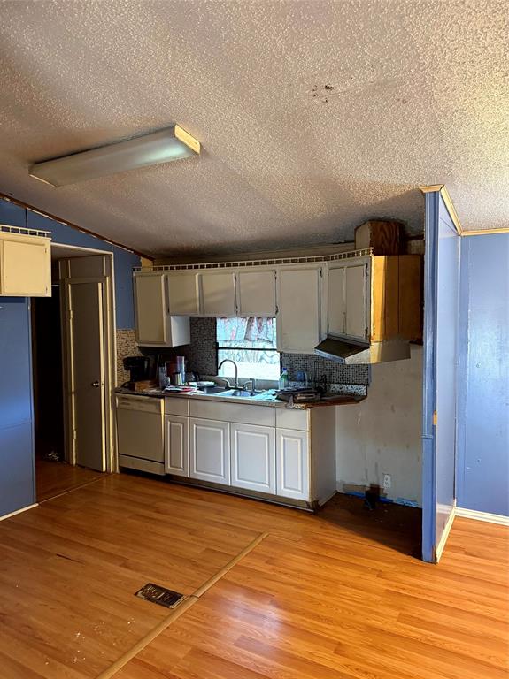 1047 John Wayne Road Kaufman, TX 75142 - Photo 13 of 17 Kitchen featuring dark countertops, light wood-style floors, white cabinetry, dishwasher, and a textured ceiling