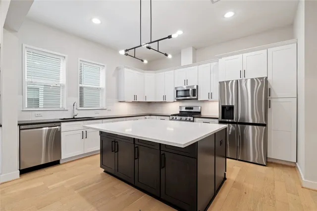 a kitchen with stainless steel appliances granite countertop a refrigerator a sink dishwasher a stove and white countertops with wooden floor