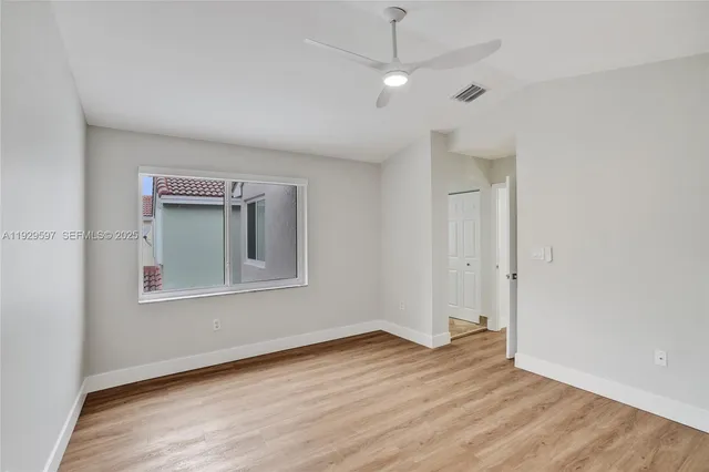 an empty room with wooden floor a ceiling fan and windows