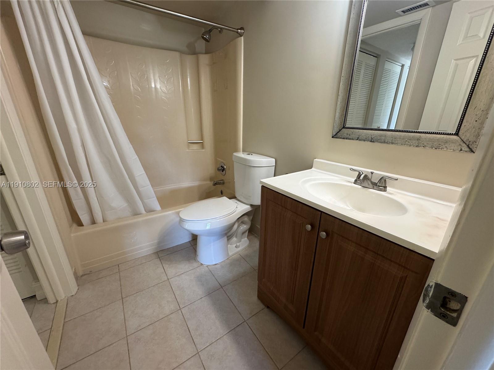 6031 Shaker Wood Circle, Unit 101 Tamarac, FL 33319 - Photo 24 of 28 a bathroom with a sink a toilet a mirror and shower curtain