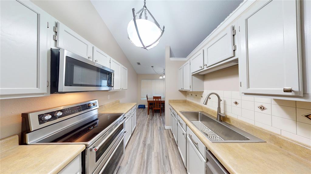 1317 Colonial Place Flower Mound, TX 75028 - Photo 6 of 20 Galley kitchen featuring white cabinetry, light countertops, stainless steel appliances, and wood-finish flooring