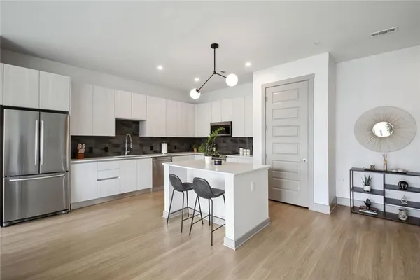 a kitchen with kitchen island granite countertop a refrigerator a stove a sink and white cabinets with wooden floor