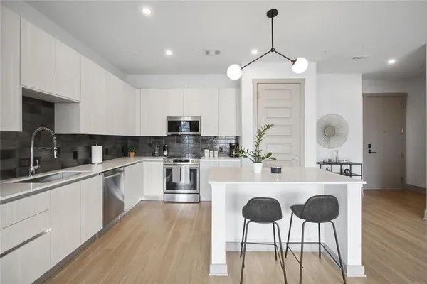 a kitchen with stainless steel appliances kitchen island granite countertop a sink a stove a refrigerator and white cabinets with wooden floor