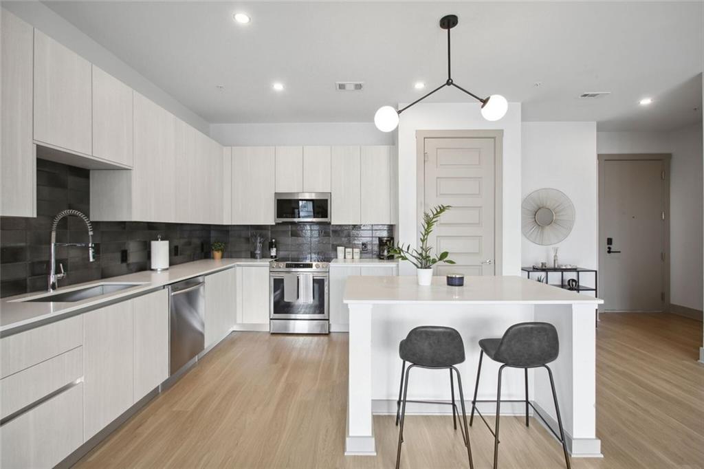 1050 Howell Mill Road, Unit 2 Atlanta, GA 30318 - Photo 5 of 17 a kitchen with stainless steel appliances kitchen island granite countertop a sink a stove a refrigerator and white cabinets with wooden floor