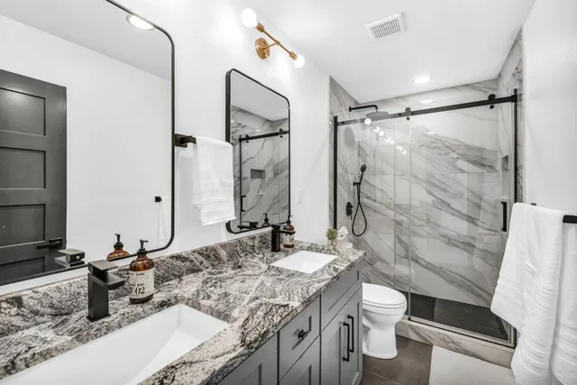 a bathroom with a granite countertop sink a toilet a mirror and shower