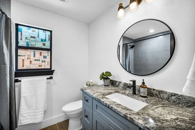 a bathroom with a granite countertop toilet a sink and a mirror