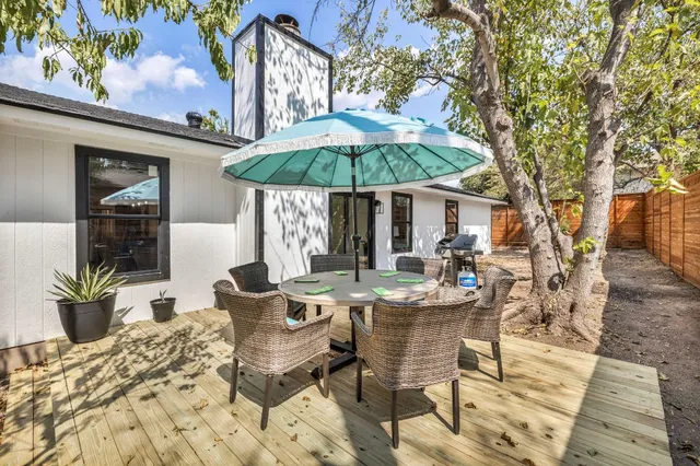 a view of a patio with table and chairs under an umbrella with a barbeque