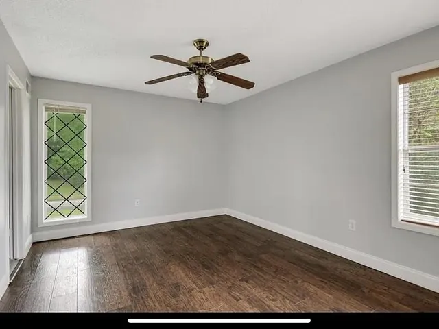 an empty room with wooden floor fan and windows