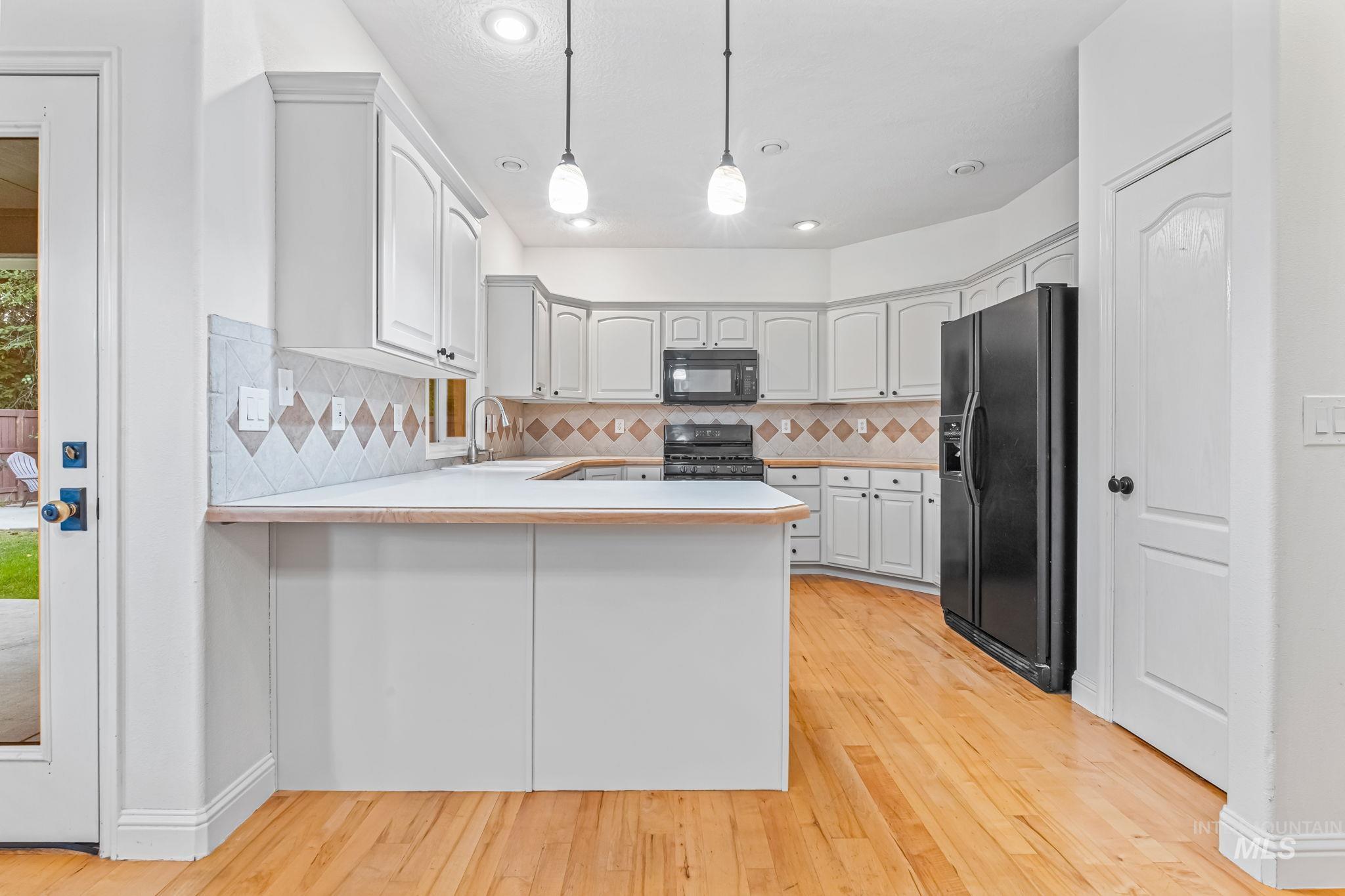 6099 North Heathrow Way Boise, ID 83713 - Photo 12 of 39 Kitchen with light countertops, hanging light fixtures, a peninsula, black appliances, and backsplash
